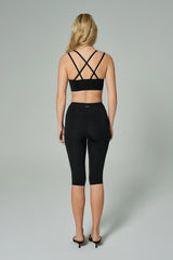 NALA Activewear black cross-back sports bra and capri leggings set back view; siyah çapraz askılı spor sütyen ve diz altı tayt giyen kadın model gri fonda arkadan görünüyor.