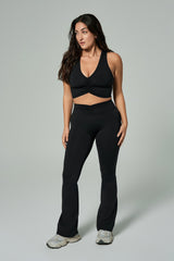 NALA Activewear black flared leggings and ruched sports bra on curvy model; siyah İspanyol paça tayt ve büzgülü spor sütyen giyen kıvrımlı kadın model gri fonda önden duruyor.