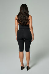 NALA Activewear black high-waist biker shorts on curvy model; siyah yüksek bel diz altı tayt şort giyen kadın model gri fonda arkadan görünüyor.